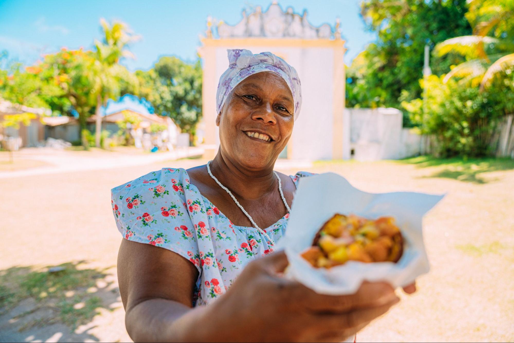 Baiana oferece acarajé em Porto Seguro. Imagem ilustrativa para post sobre pontos turísticos no ES e na BA, do blog da Soma Urbanismo.